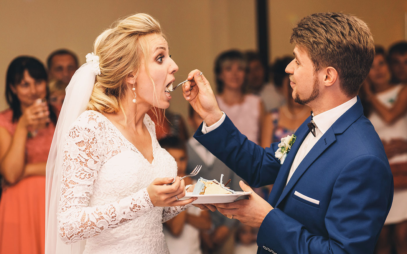 Bride opens her mouth broad tasting wedding cake from groom's fo